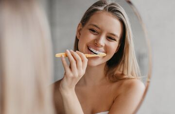 Woman brushing teeth in mirror